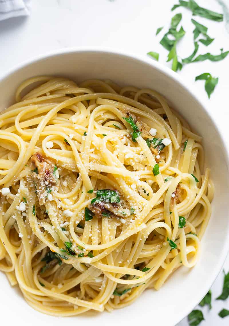 A bowl of linguine aglio e olio with roasted garlic, garnished with fresh minced parsley.