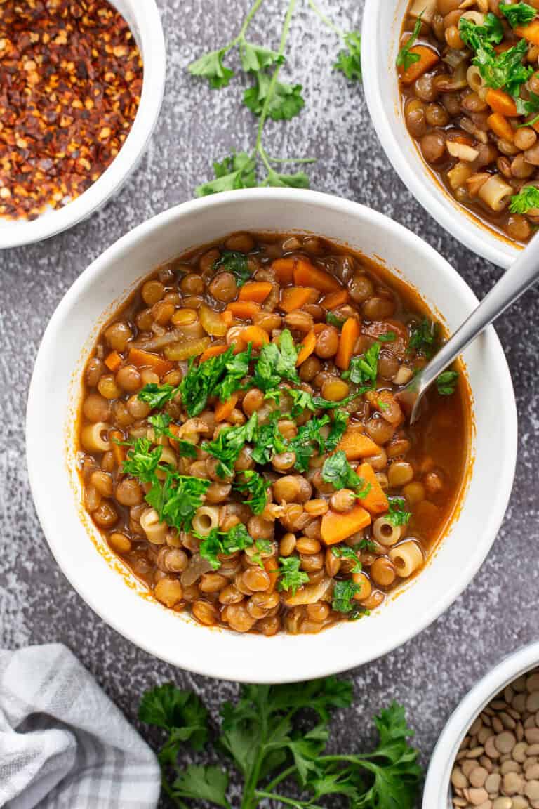 A bowl of lentil soup with a spoon in it and garnished with fresh parsley.