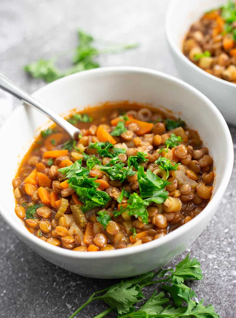 A bowl of lentil soup topped with fresh parsley and surrounded by small sprigs of it.