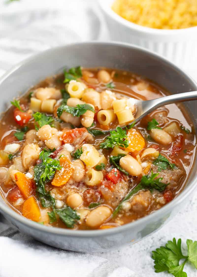 A bowl of pasta e fagioli soup, garnished with fresh parsley. A spoon is also placed in the bowl.