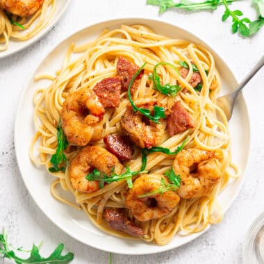 Plate of pasta with shrimp, chorizo, and arugula with a fork digging into it.