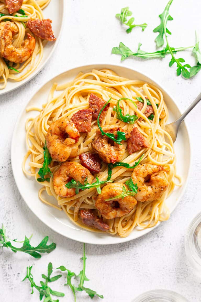 Plate of pasta with shrimp, chorizo, and arugula with a fork digging into it.