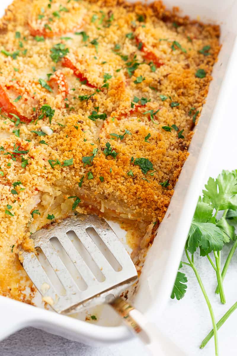 A potato-tomato casserole with Gruyere, topped with crispy panko with a piece cut out.