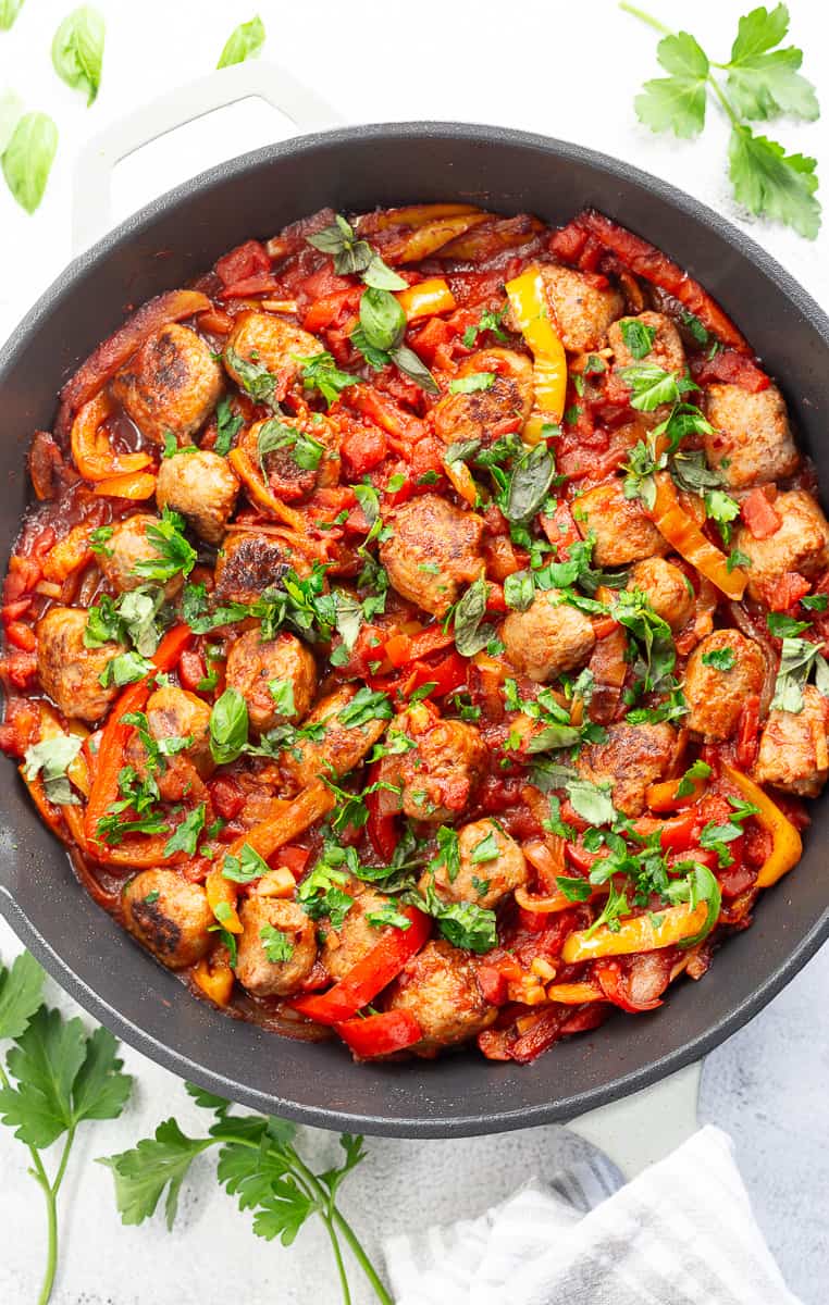 A large skillet of Italian sausage and peppers, garnished with fresh parsley.