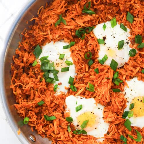 A pan of shredded sweet potatoes with chorizo and eggs and garnished with scallions.