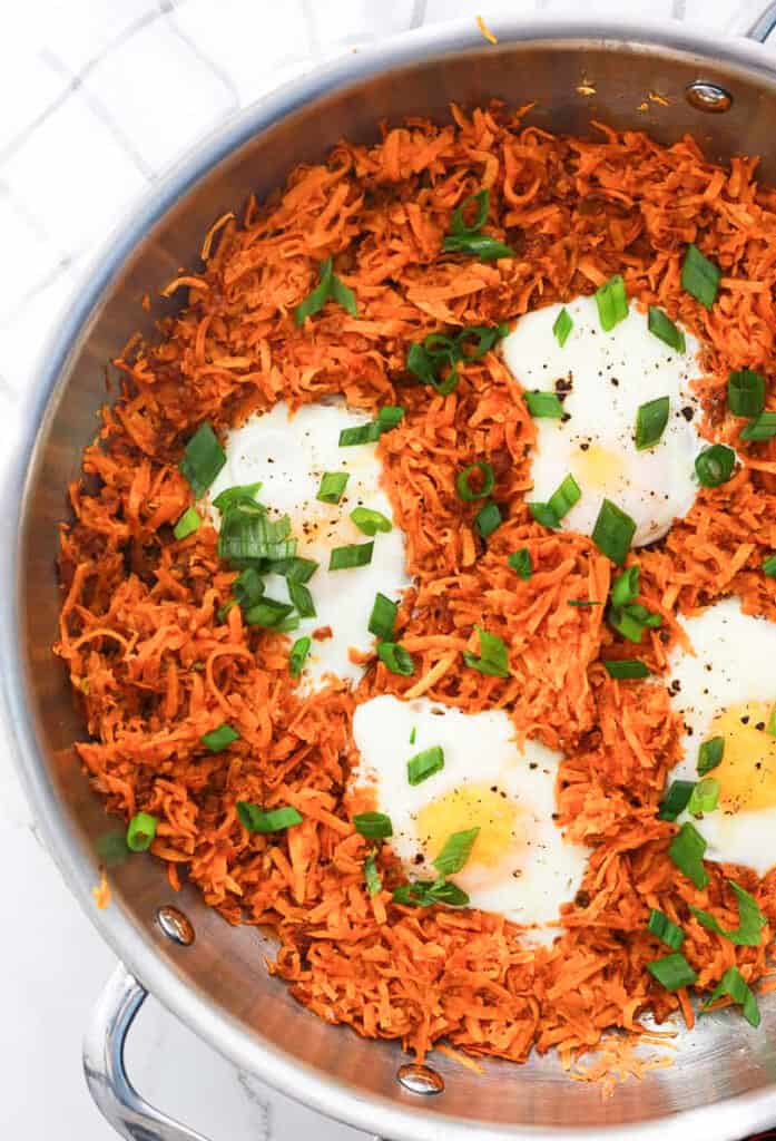 A pan of shredded sweet potatoes with chorizo and eggs and garnished with scallions.