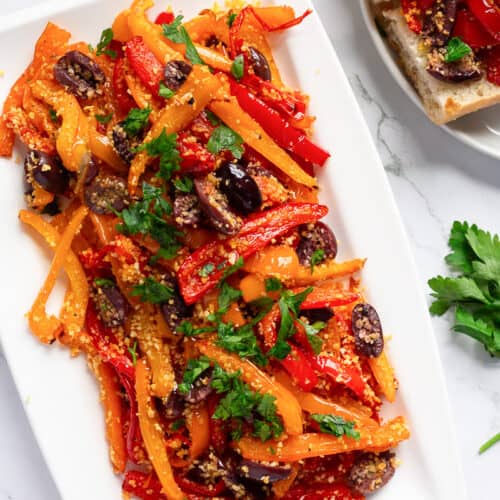 A white platter with tri-colored roasted peppers, Kalamata olives, and Panko breadcrumbs.