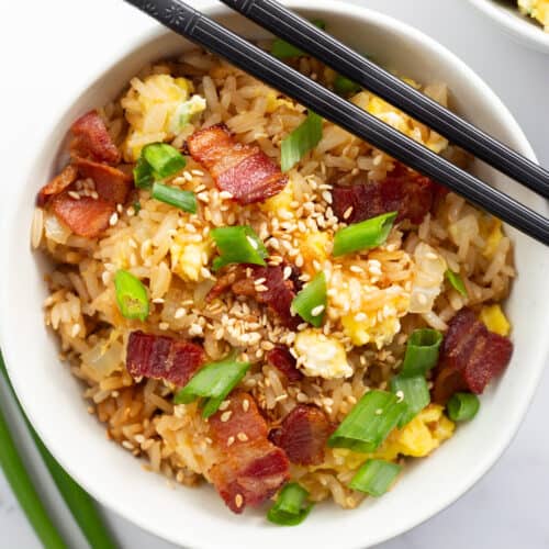 Bacon and egg fried rice in a white bowl with chopsticks resting on top of it.