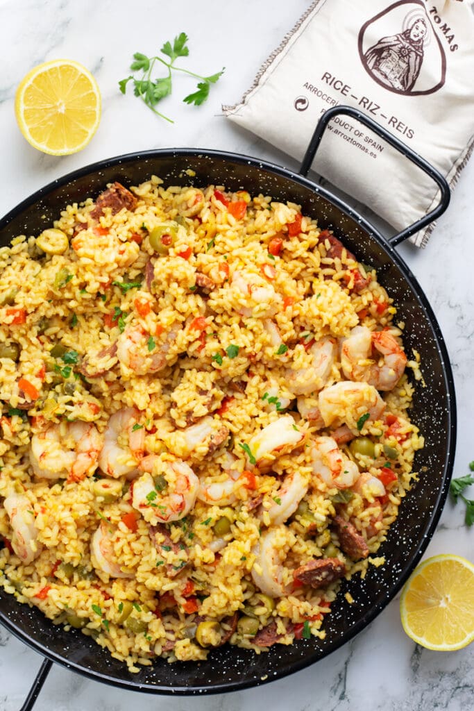 A large skillet of shrimp and chorizo paella, with two lemon wedges placed next to it.