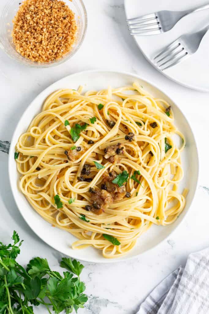 A plate of pasta with fried capers and garlic garnished with minced fresh parsley.