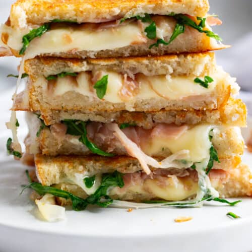 A stack of white pizza panini filled with melted provolone, prosciutto, and arugula.