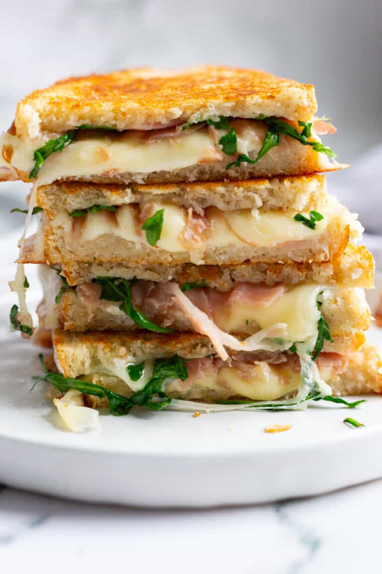 A stack of white pizza panini filled with melted provolone, prosciutto, and arugula.