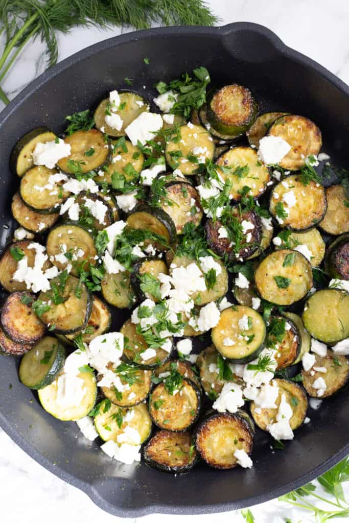 A cast-iron pan loaded with sliced zucchini with vinegar and feta.