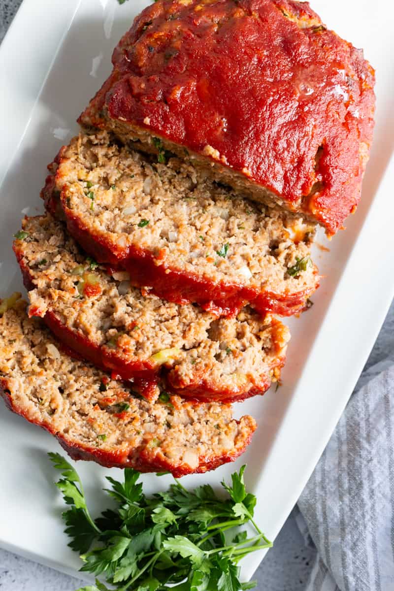 A platter of sliced meatloaf decorated with a sprig of fresh parsley.