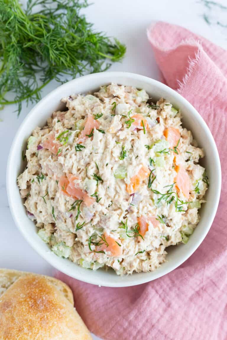 Smoked salmon tuna salad in a bowl surrounded by some Italian bread and sprigs of fresh dill.