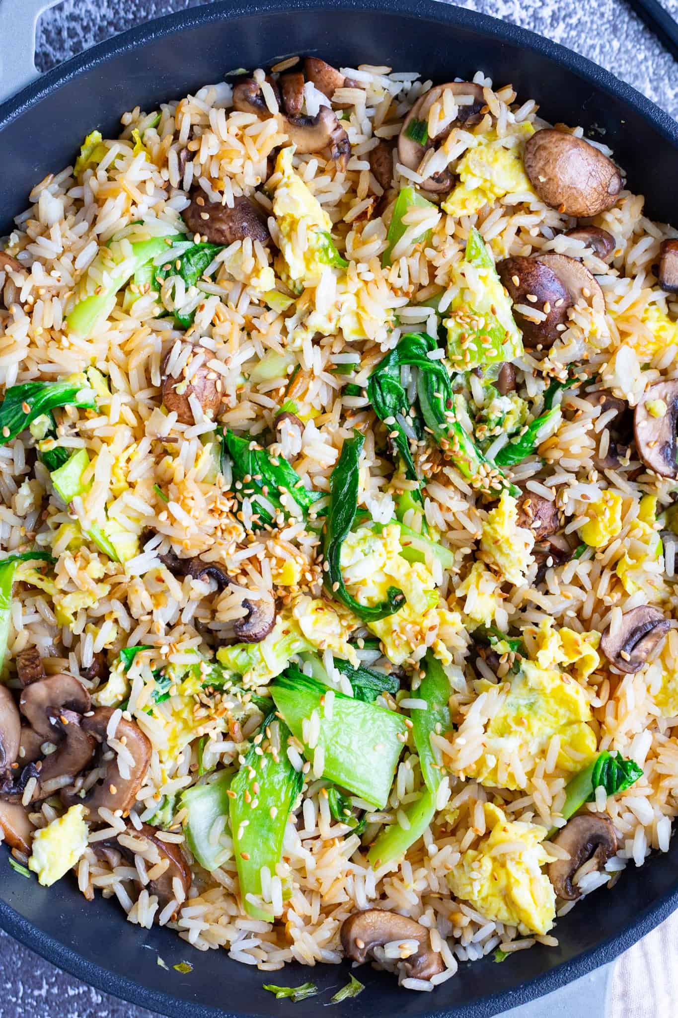 A large skillet of bok choy fried rice with mushrooms and scrambled eggs.