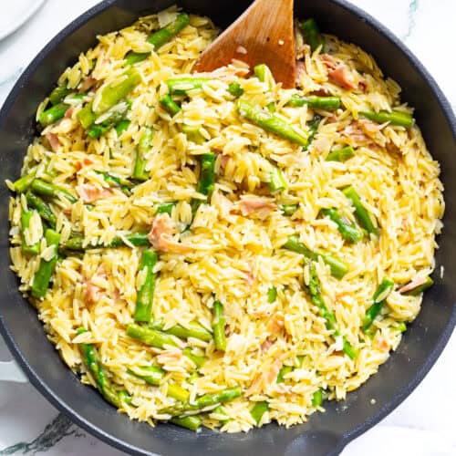 Orzo with asparagus and Parmesan in a cast-iron pan with a wooden spoon.