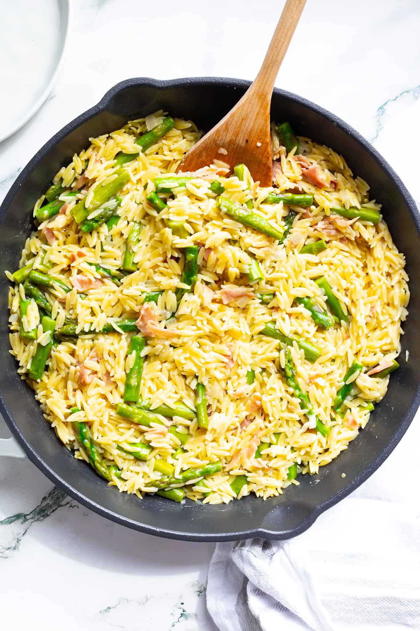 Orzo with asparagus and Parmesan in a cast-iron pan with a wooden spoon.