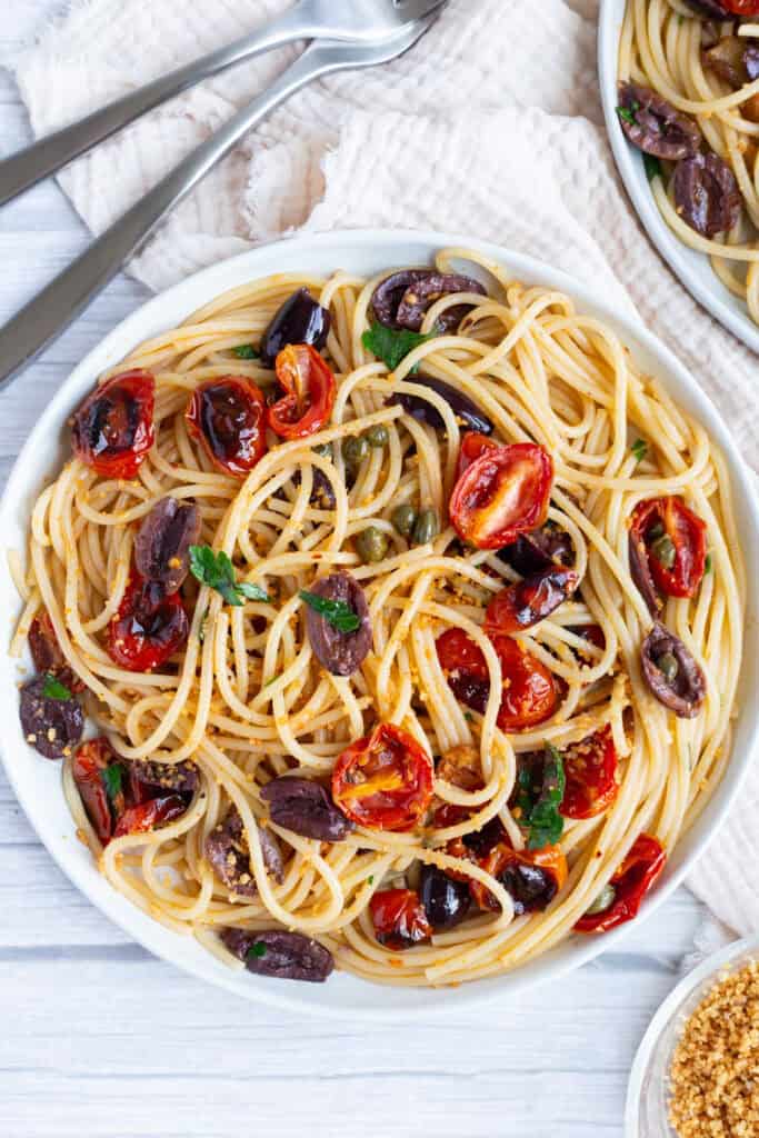 A white plate of roasted tomato linguine Puttanesca with olives and capers.