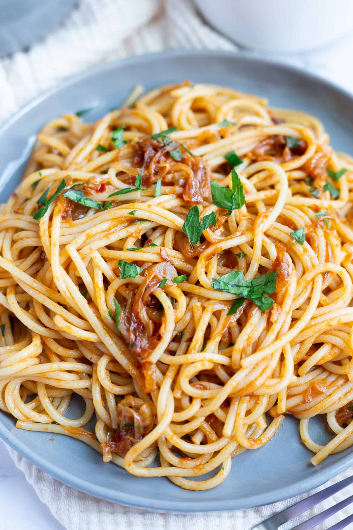 A plate of caramelized shallot pasta on a plate, with garlic and anchovies and garnished with fresh parsley.