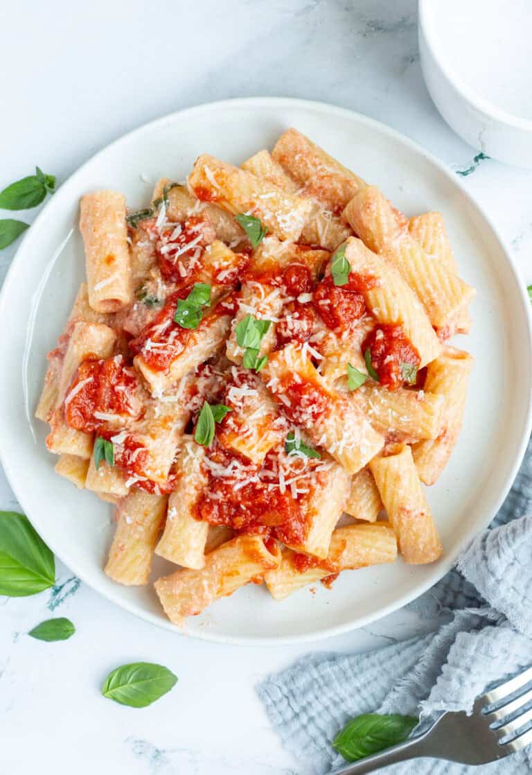 A white plate containing pasta with ricotta cheese and surrounded by torn fresh basil.