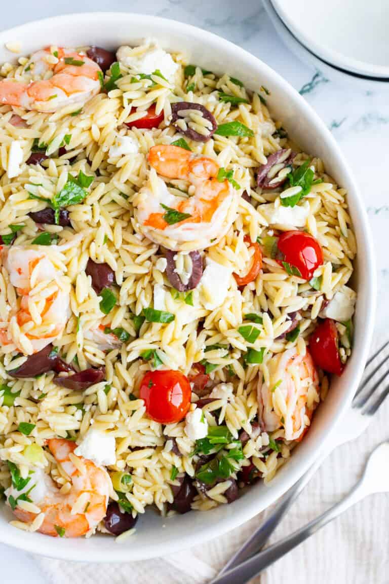 A large bowl filled with orzo, shrimp, cherry tomatoes, olives, and feta.