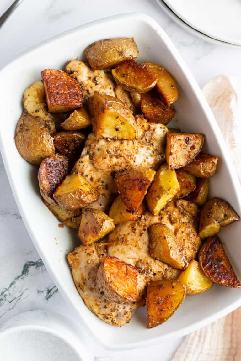 A white platter of baked vinegar chicken thighs and potatoes.