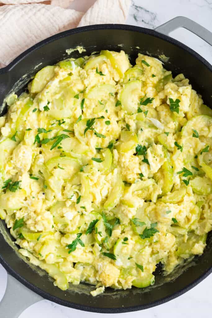 A skillet of cooked zucchini and scrambled eggs, garnished with minced fresh parsley.