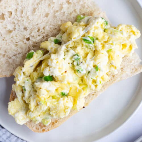 An open-faced hoagie roll filled with eggs and mozzarella on a white plate.