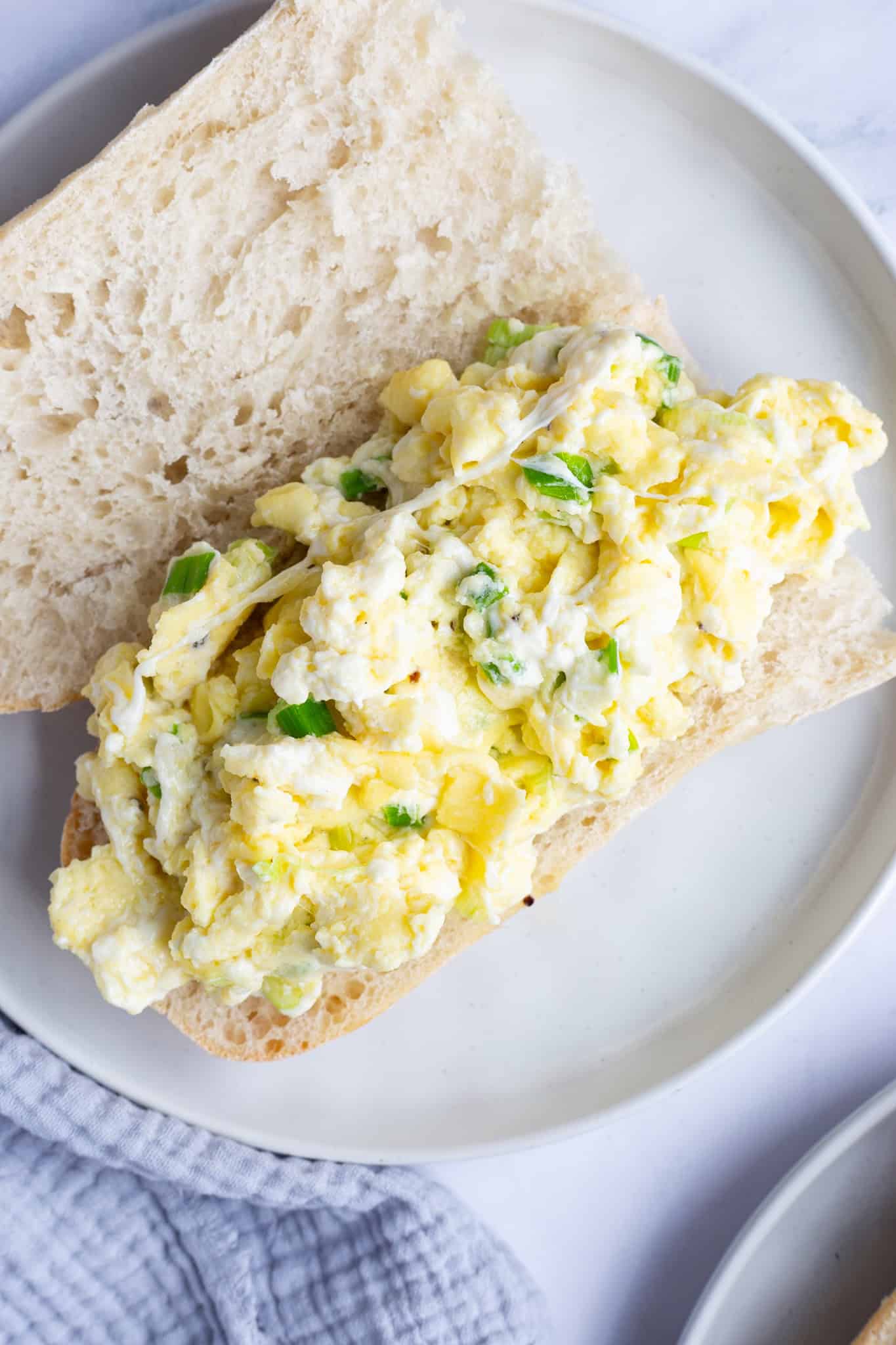 An open-faced hoagie roll filled with eggs and mozzarella on a white plate.