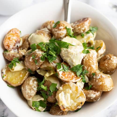 A small white bowl filled with creamy potatoes and artichokes and garnished with fresh parsley.