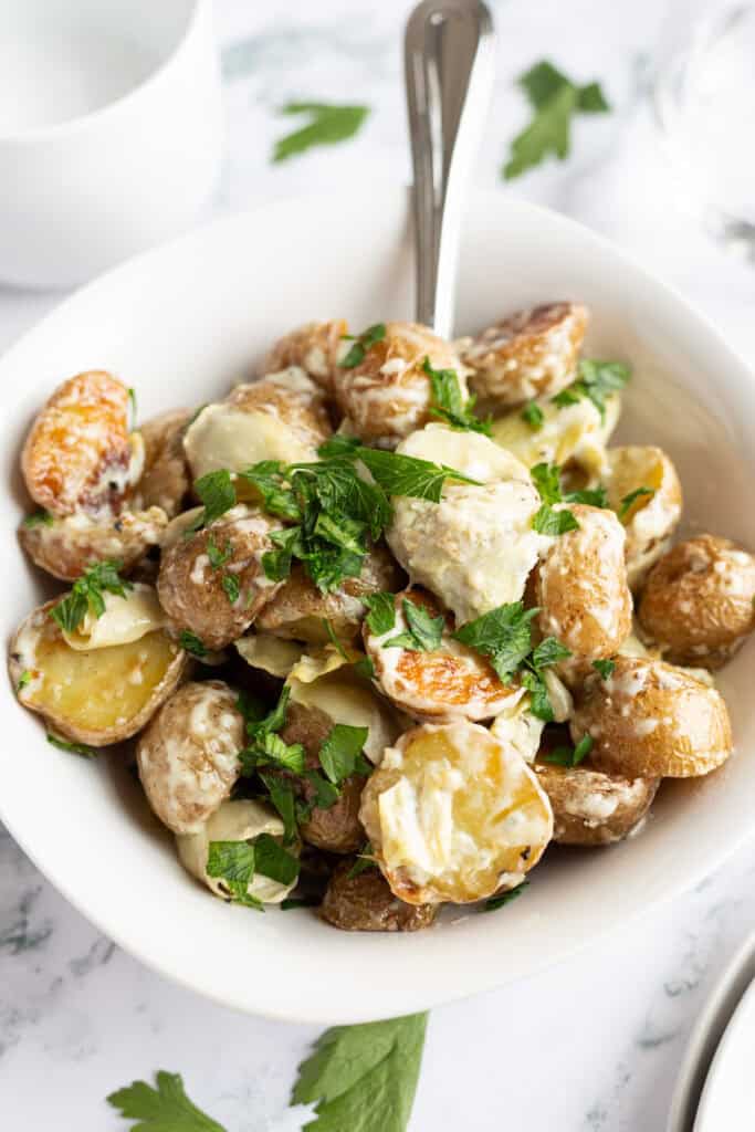 A small white bowl filled with creamy potatoes and artichokes and garnished with fresh parsley.