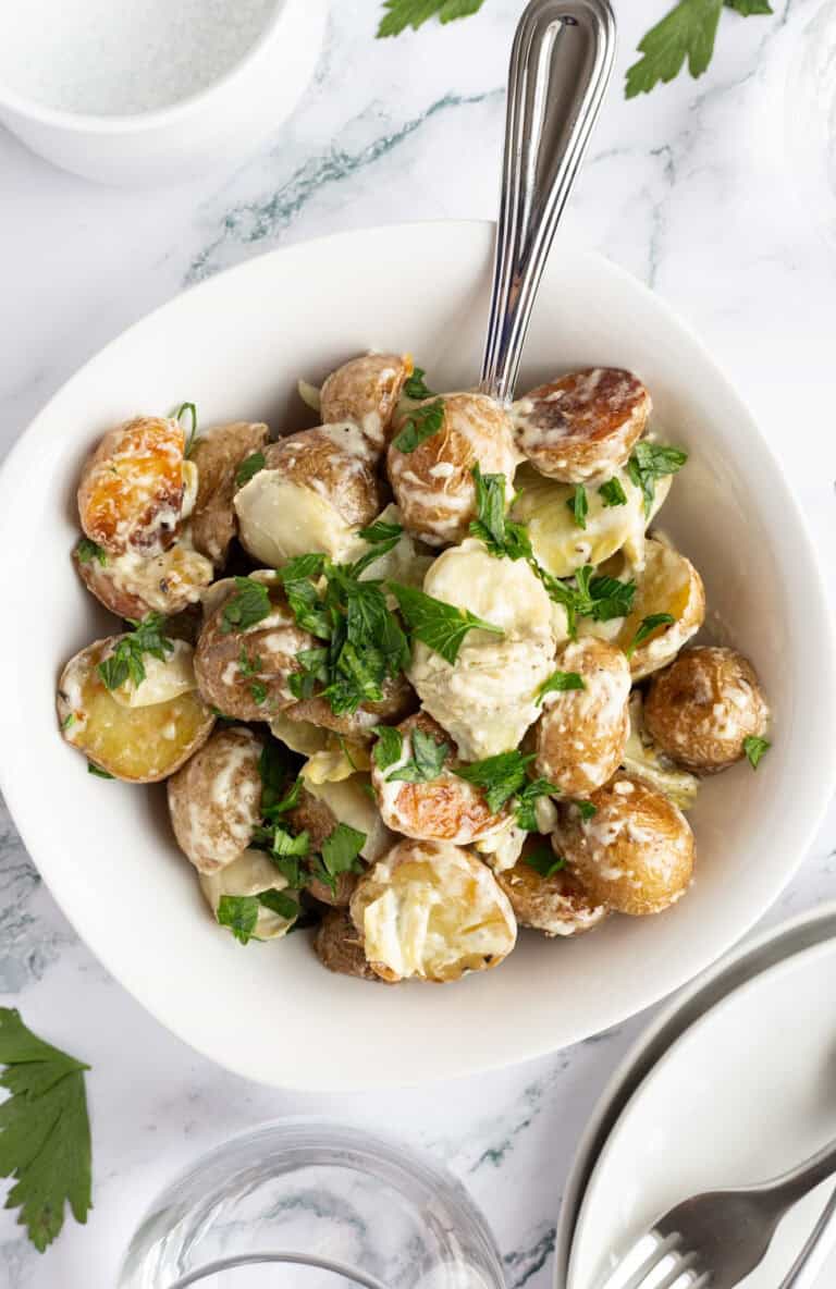 A bowl of potatoes and artichokes with a serving spoon sticking from it.