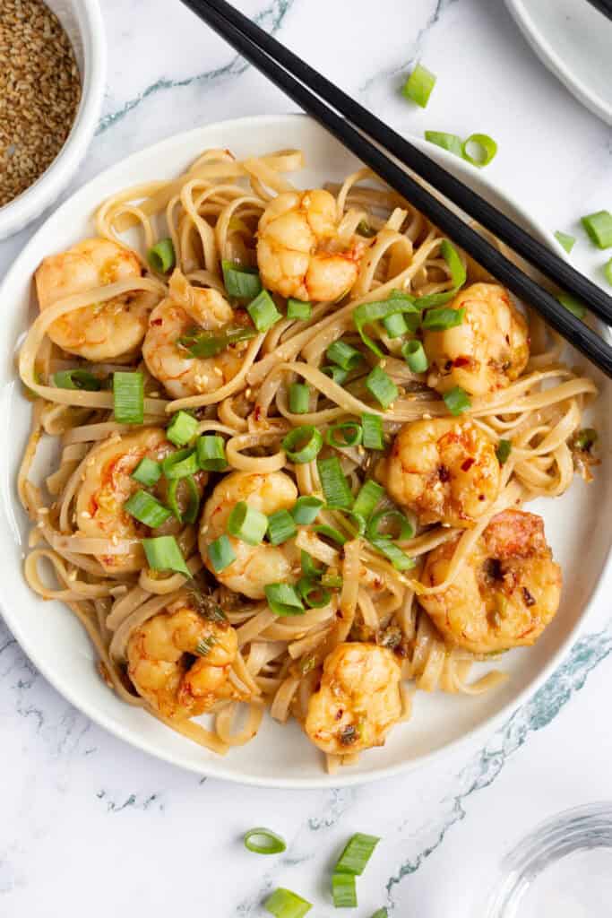 Plate of ginger-scallion noodles with shrimp, garnished with scallions.