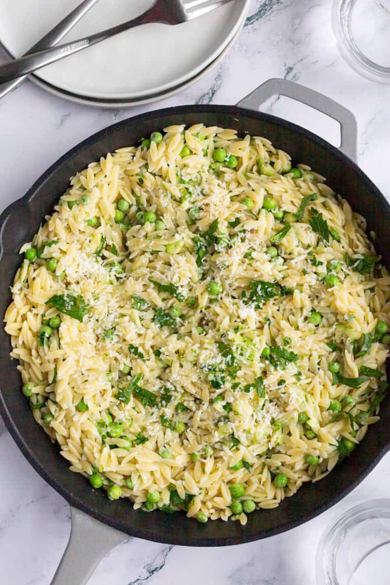 A large skillet filled with zucchini orzo and garnished with fresh minced parsley.