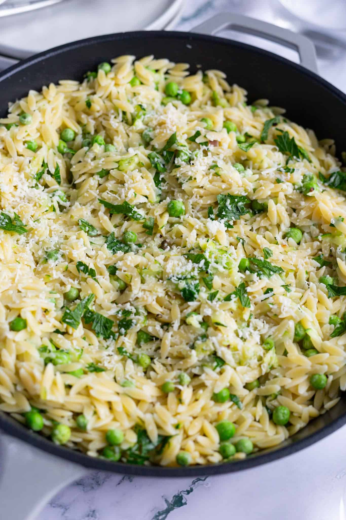 Large cast-iron pan filled with zucchini orzo and garnished with Pecorino and fresh parsley.