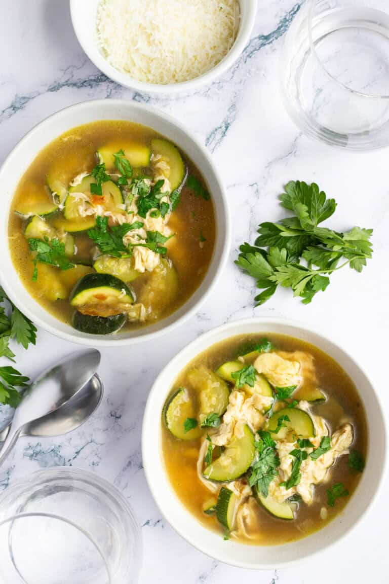 Two bowls of Italian zucchini soup accompanied by a small bowl of Pecorino Romano cheese.