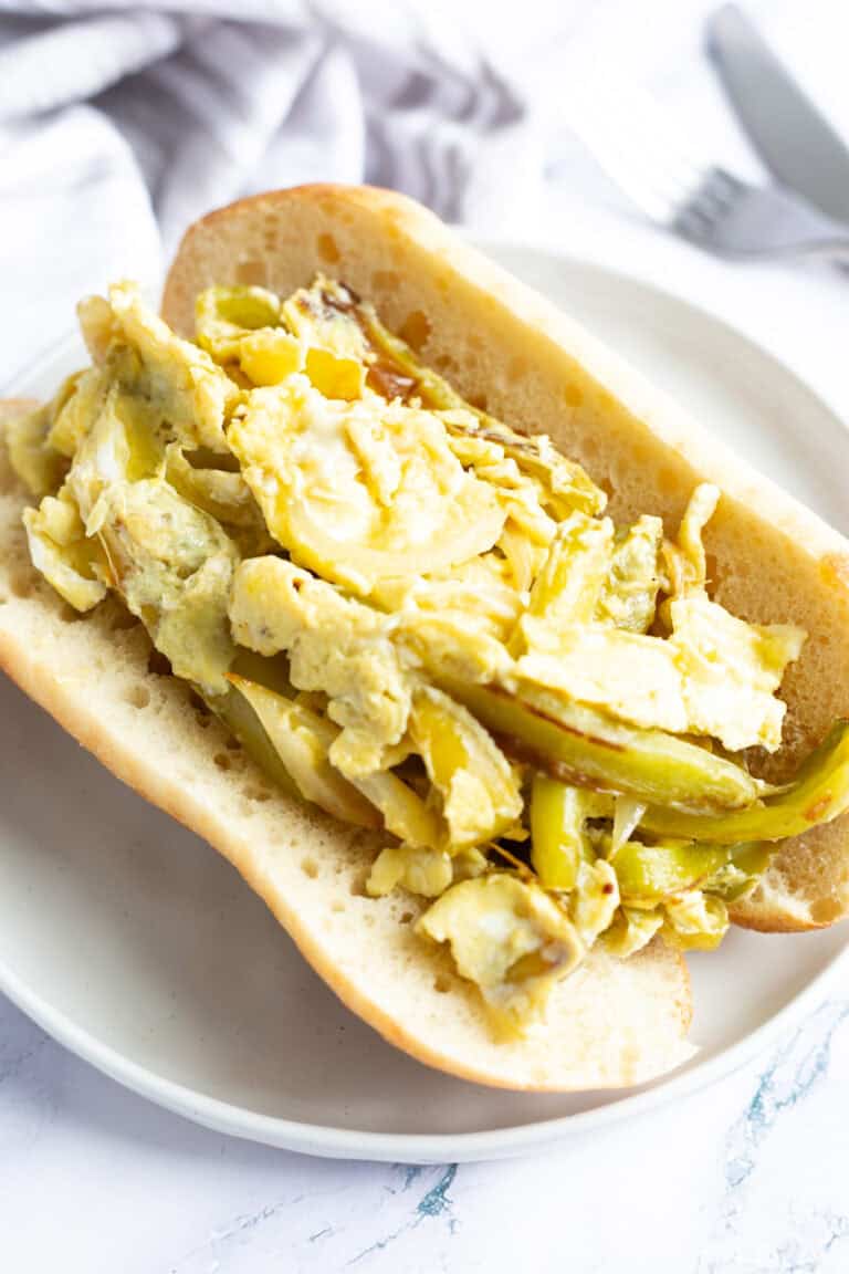 A peppers and egg sandwich on Italian-style bread and served on a white plate.