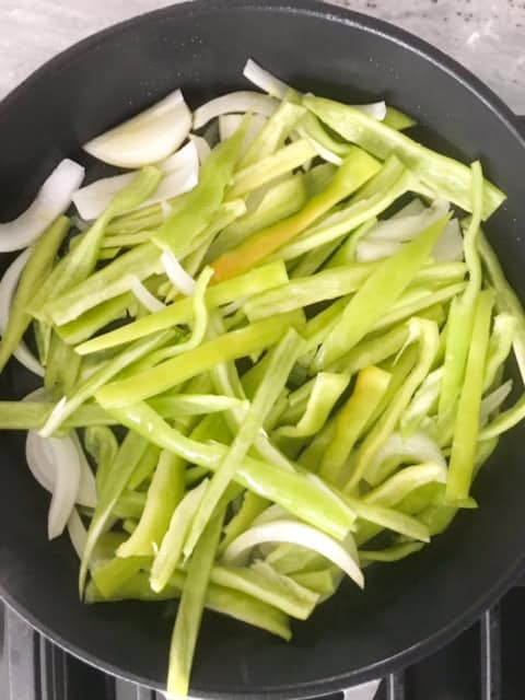 Peppers and onions cooking in pan.