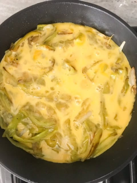 Eggs added to cooked peppers and onions in pan.