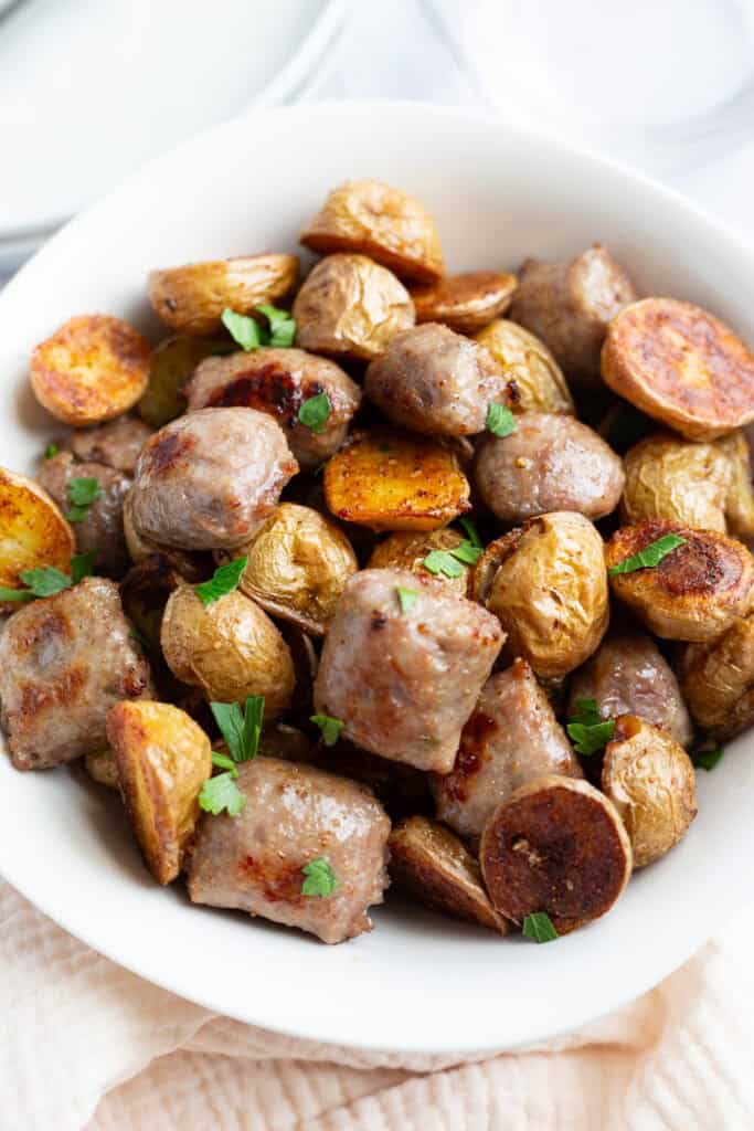 A white bowl filled with golden-brown sausage and potatoes.