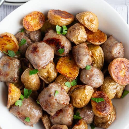 A bowl of Italian sausage and potatoes garnished with minced fresh parsley.