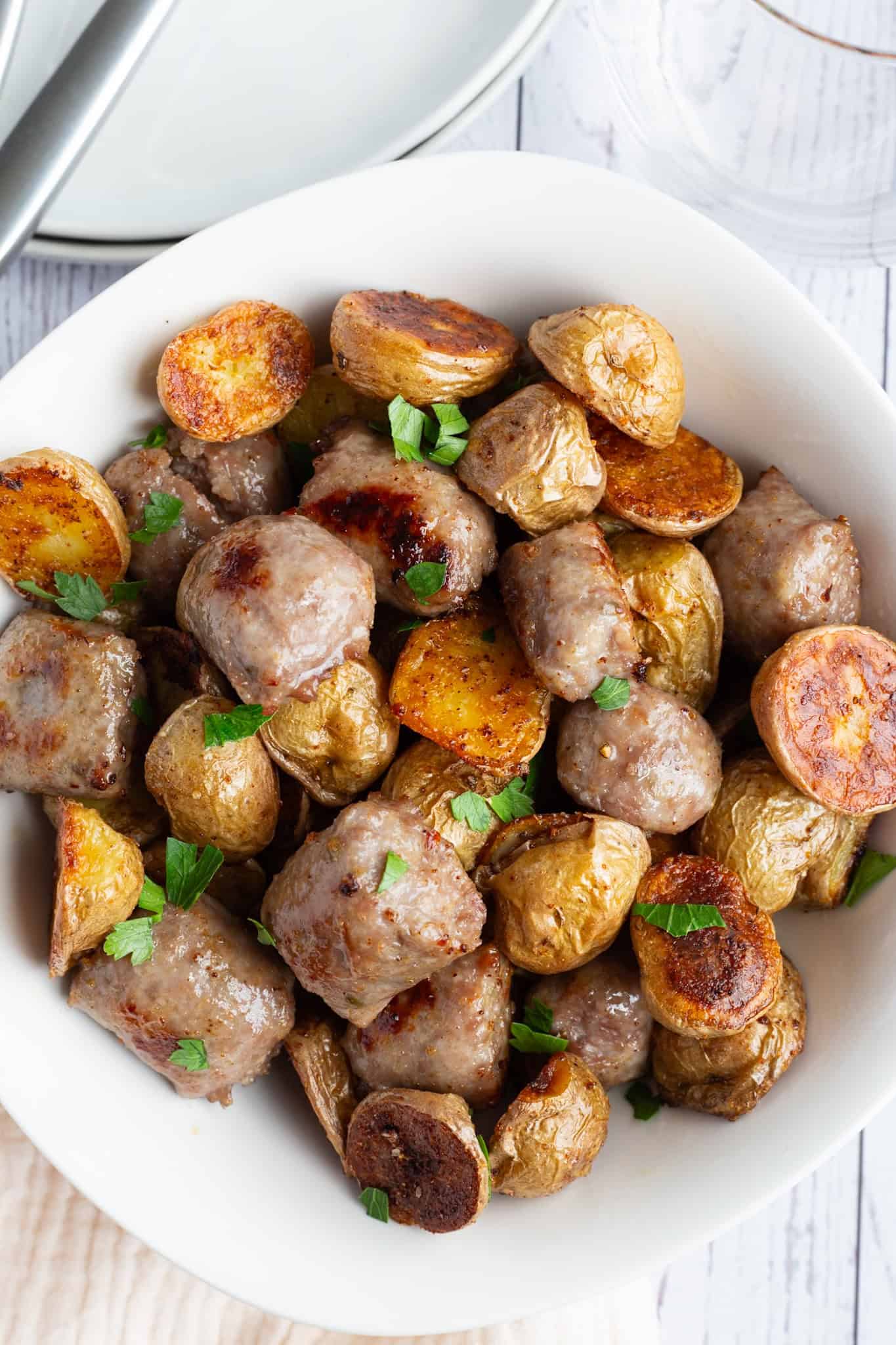 A bowl of Italian sausage and potatoes garnished with minced fresh parsley.