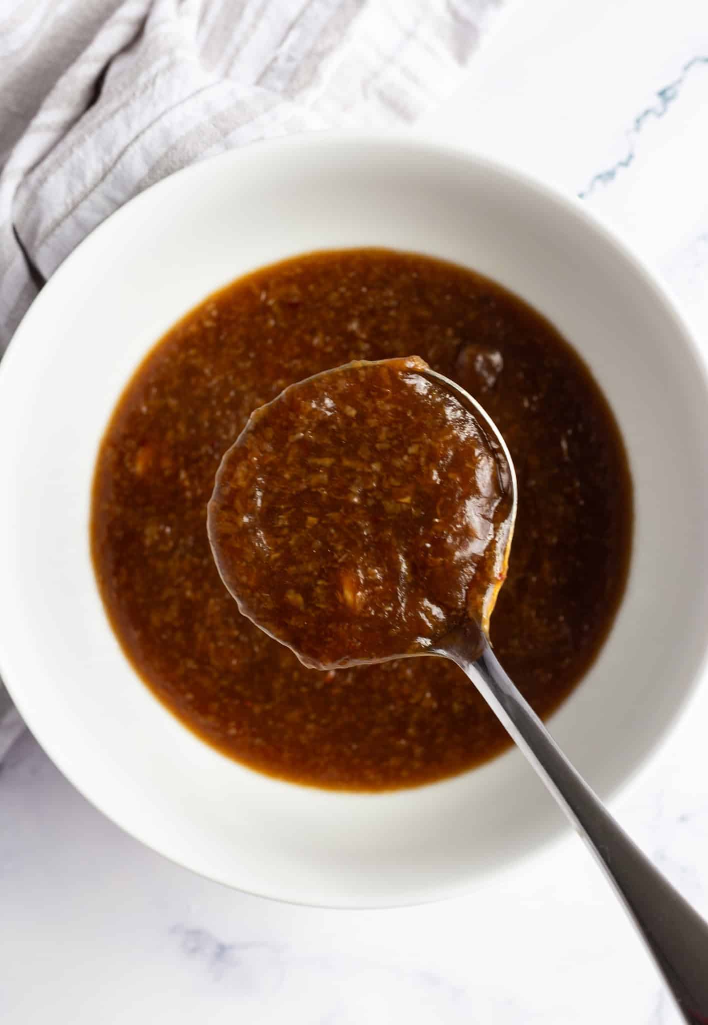 A ladle filled with Asian garlic sauce above a bowl filled with more of the sauce.