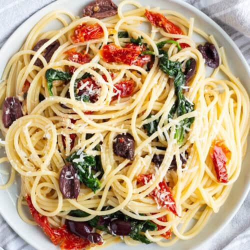 A plate of kalamata olive pasta with sun-dried tomatoes and wilted spinach.