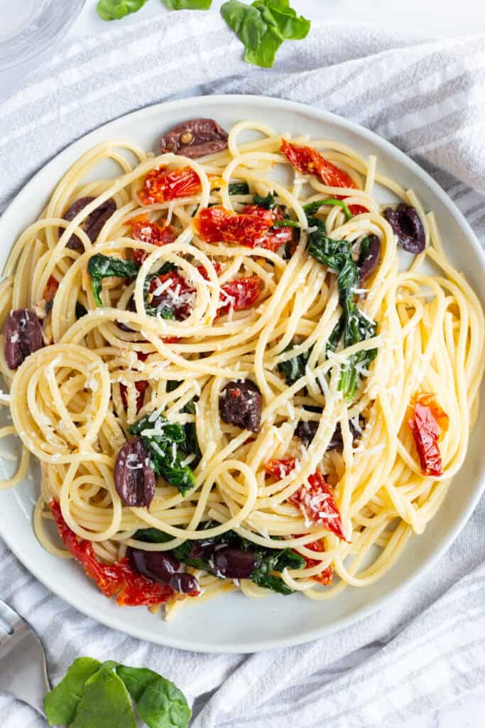 A plate of kalamata olive pasta with sun-dried tomatoes and wilted spinach.