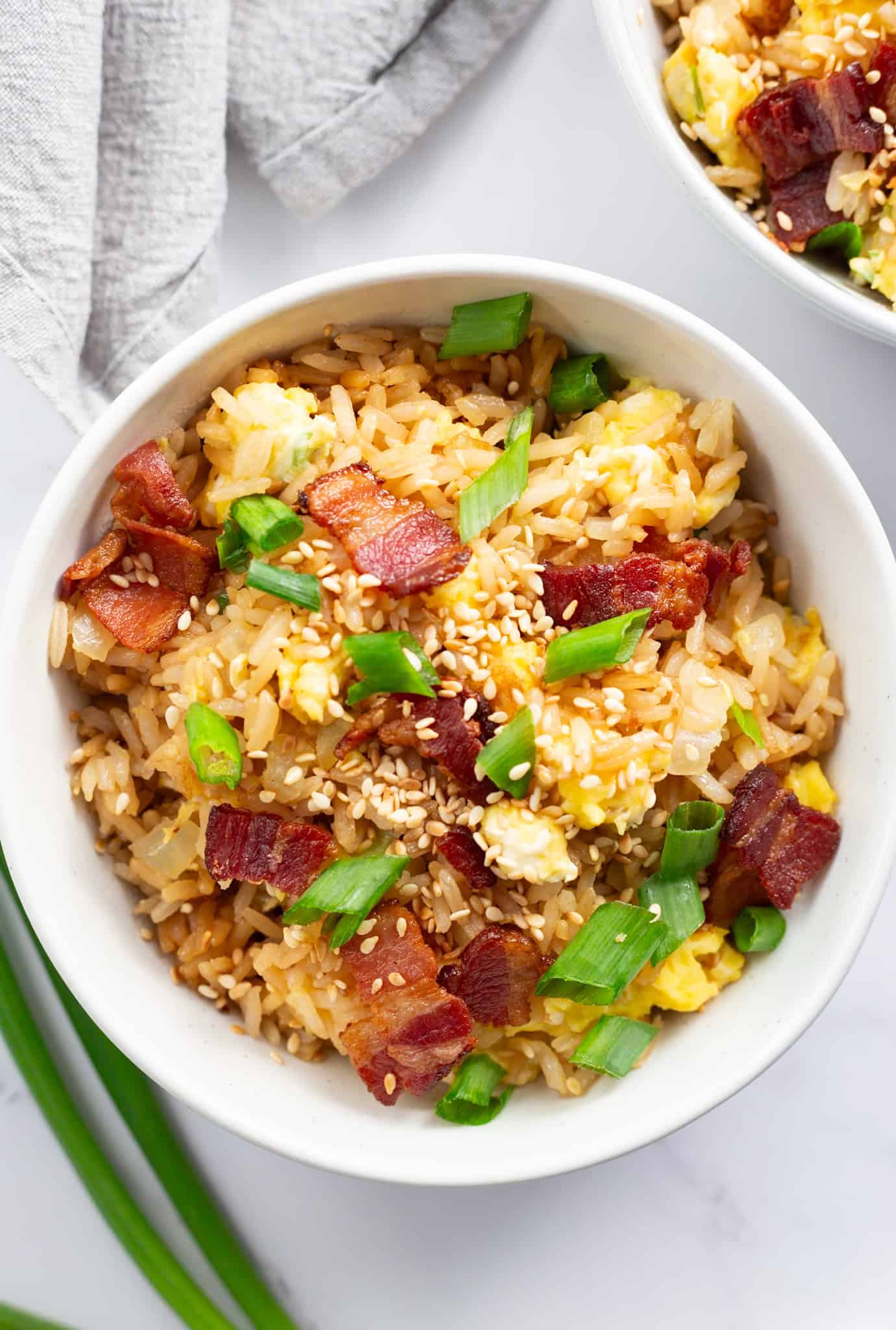 A bowl of bacon and egg fried rice garnished with lots of scallions and sesame seeds.