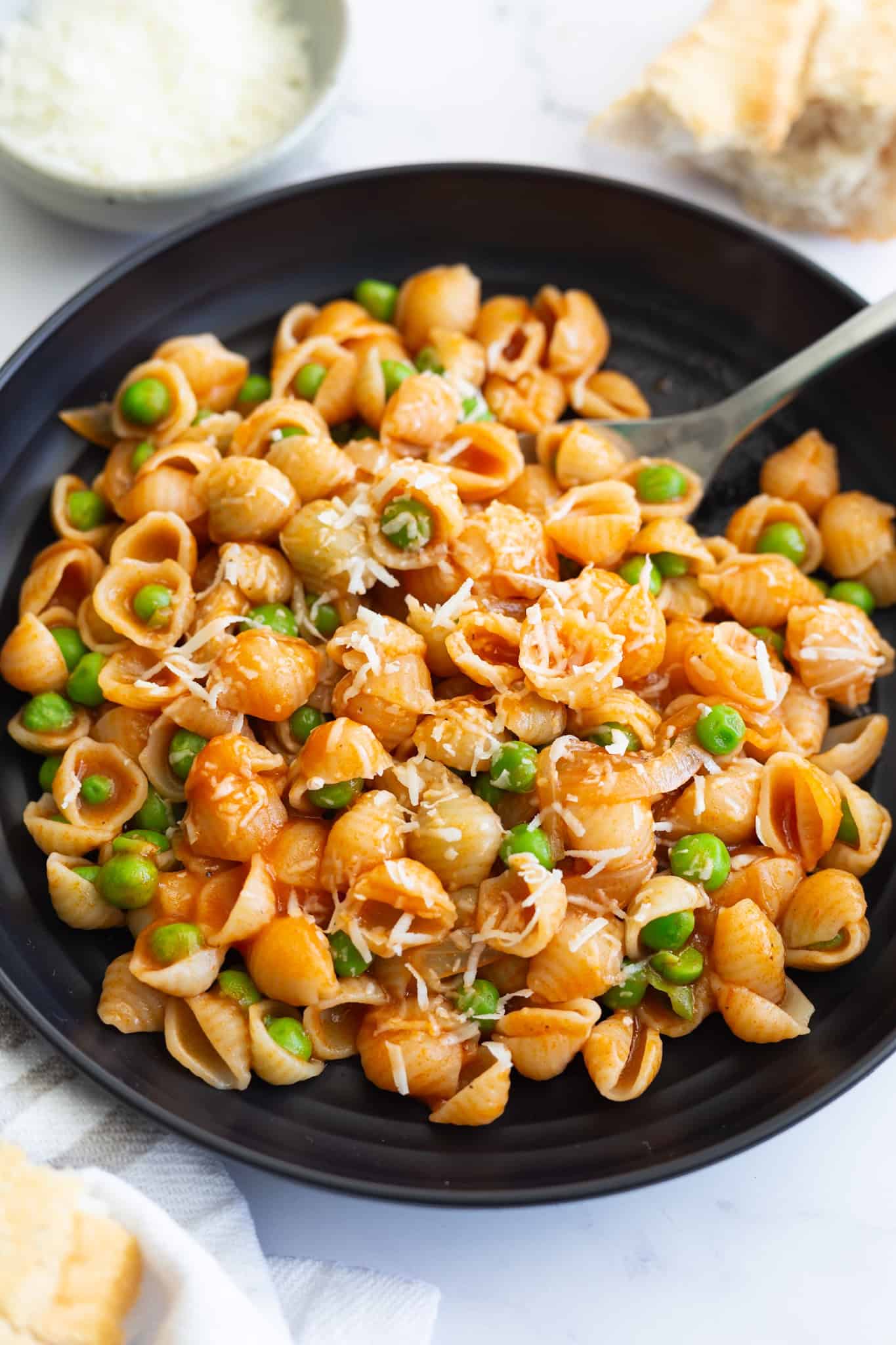 A bowl of peas with small pasta shells in red sauce. A spoon is also in the bowl.