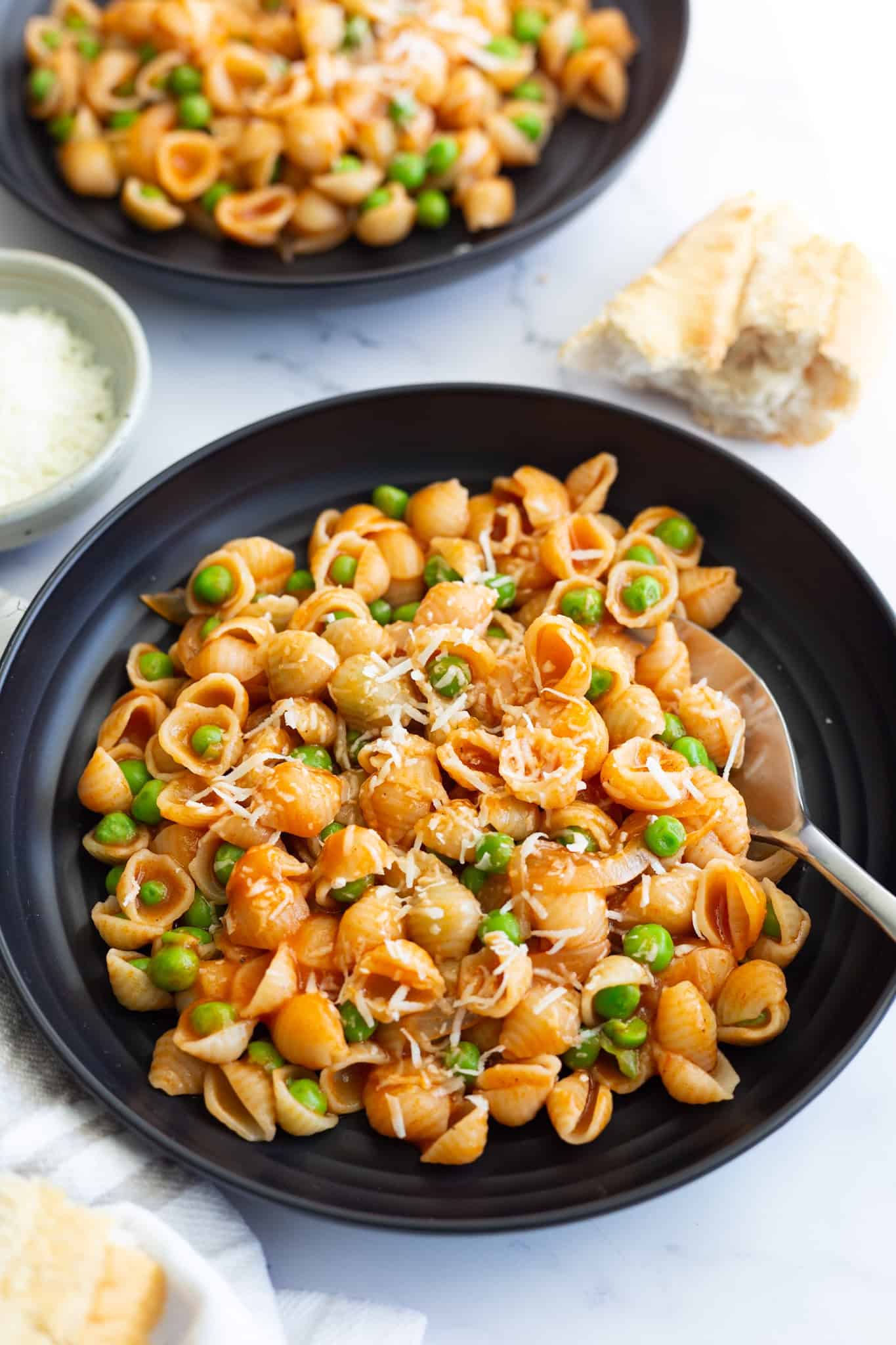 A dark plate with small  pasta shells cooked with green peas. 