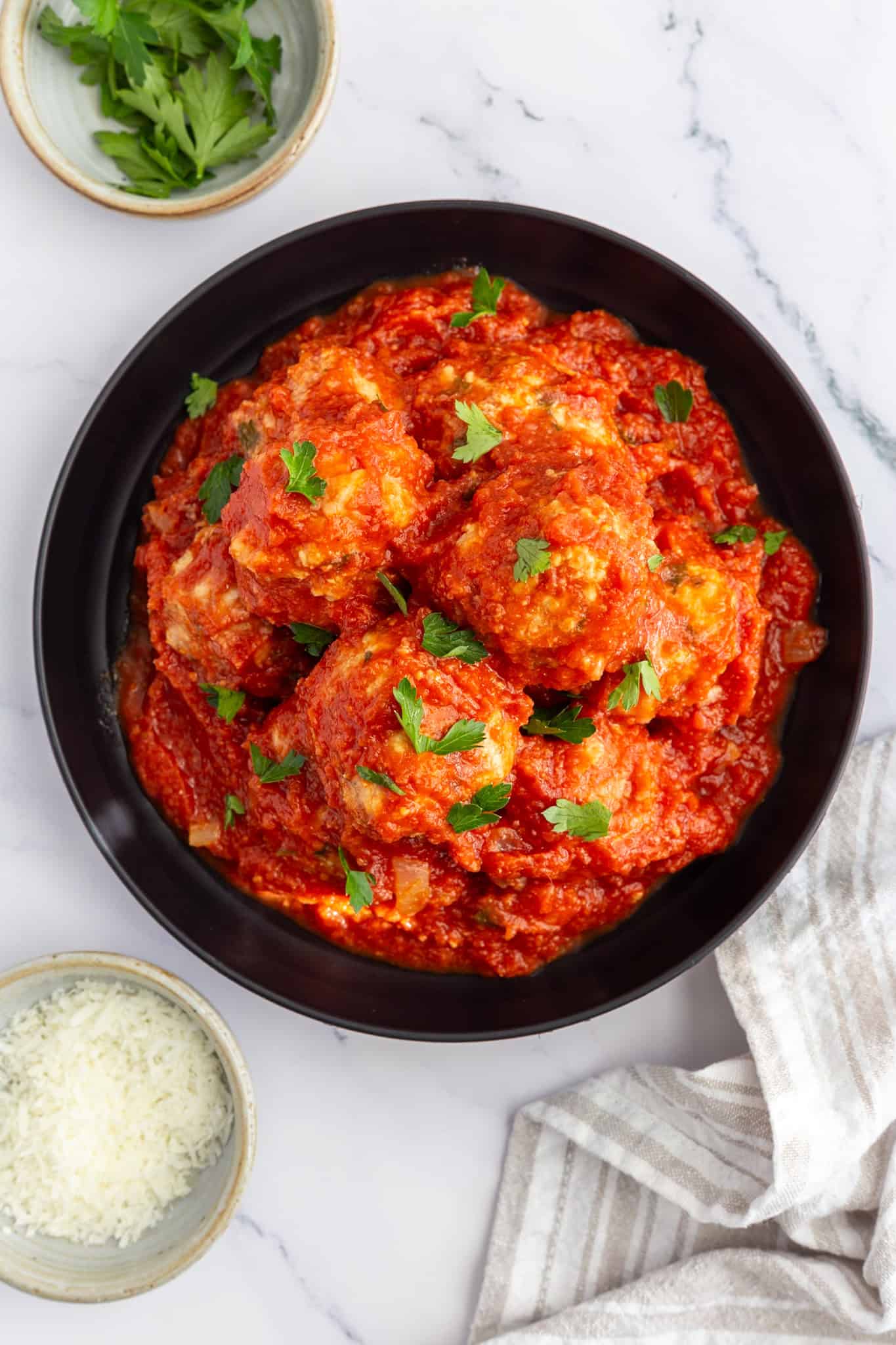 A black plate filled with classic Italian meatballs cooked in marinara sauce.